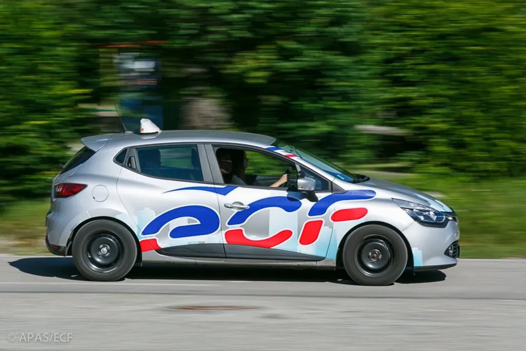 Voiture d’auto-école aux couleurs bleu, blanc et rouge du réseau ECF, en circulation sur une route de campagne